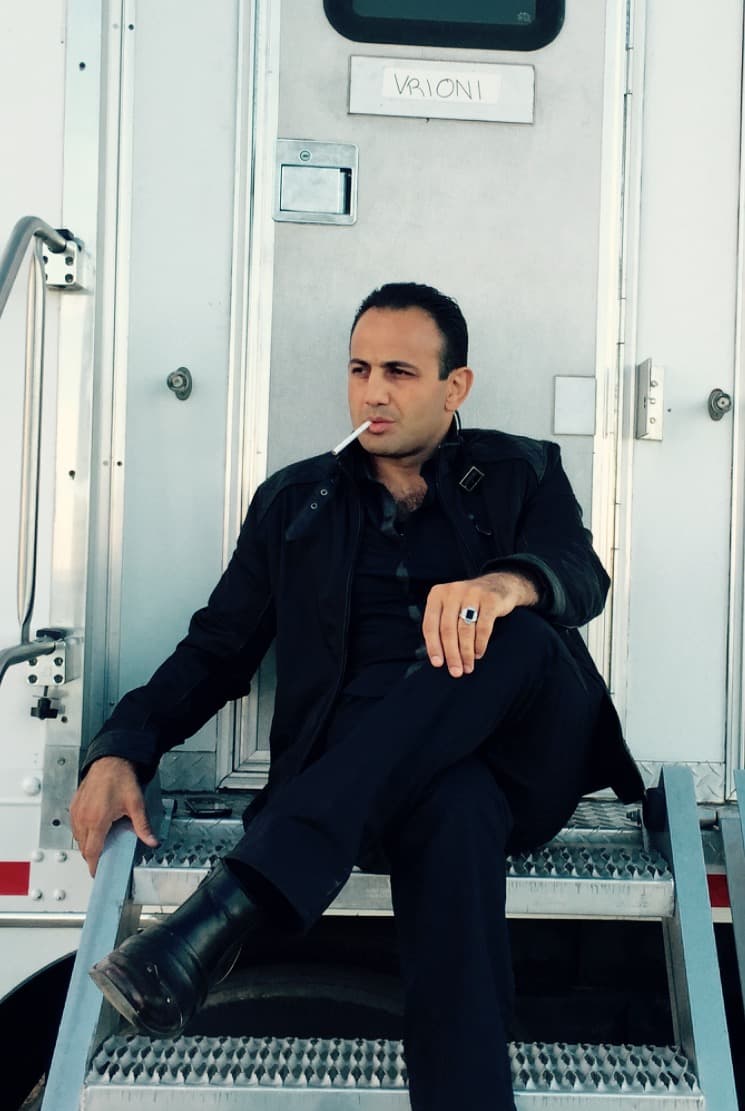 Roman Mitichyan dressed in black, seated on the steps of a location trailer