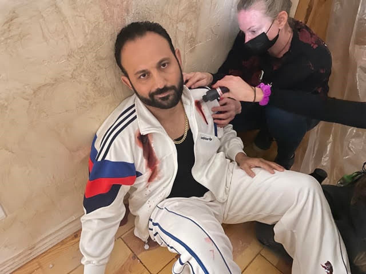Roman Mitichyan in a white tracksuit having special-effects makeup applied between takes
